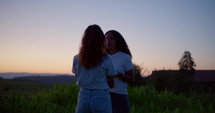 Two girls praying  and hugging at dusk in a field 4