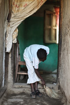woman sweeping the dirt floor of her house in Ethiopia 
