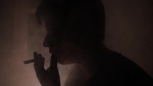 Troubled young man, teenage boy smoking drugs or cigarette, getting high, in dark, smoky room in cinematic slow motion lighting joint.