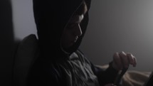 Young, sad, depressed man, teenage boy sits alone in a dark room smoking a cigarette or drugs like marijuana.