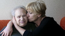 Middle aged woman kissing an elderly woman on the cheek.