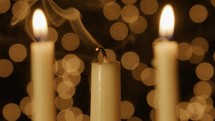 Lit taper candle getting blown out with Christmas light bokeh in the background. 