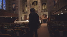 hooded man walking into an empty church 
