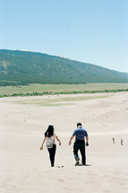 couple walking down sand dunes 