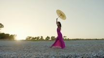 Girl in pink dress and yellow umbrella Dance On the Beach At Sunset