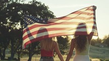 young woman walking with an American flag draped over their backs 