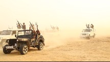 men with rifles riding in trucks through the desert 