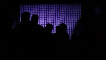 silhouettes of a production crew walking in front of netting 