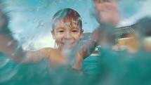 Slow motion of a child playing in the pool. Happy boy having fun on vacation. Close-up shot of water splashes