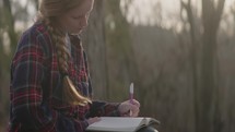 Smiling young woman reading her bible, writing notes, and admiring nature