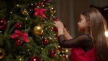 young baby girl putting a red ball to decorate Christmas tree 