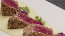 Chef is serving crusted tuna fillets with sesame seeds on a sauce