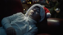 Kid with Christmas hat falling asleep under the tree