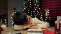 Child sleeping on his desk under Christmas tree 
