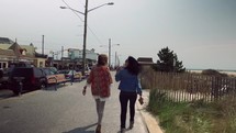 women walking down a sidewalk heading to a beach 