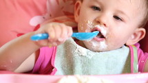 messy face of a toddler girl eating with a spoon in a highchair 