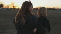 a woman carrying her toddler son outdoors at sunset 