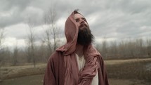 Jesus Christ dressed in brown robes and shroud in the wilderness temptation by the Devil or Satan for 40 days and 40 nights looks up to God in heaven in stoic, prayerful contemplation. Could also be used to depict a biblical prophet like Noah, Abraham, Elijah, Moses or John the baptist. 