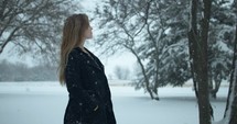 Woman in winter coat walking outside on Christmas watching slow motion snow as snowflakes fall in cinematic slow motion.