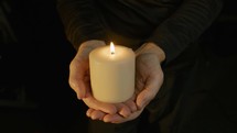 Man holding a lit pillar candle in his hands.