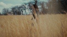 a woman walking through a field of tall brown grasses 
