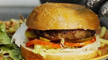 Large hamburger placed on a bun with vegetables in slow motion.