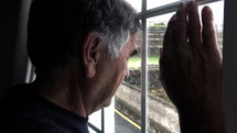 Older man resting his forehead against a window.
