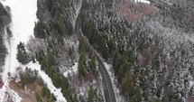 Aerial, tilt up, drone shot, of a road in middle of snowy spruce forest, on a mountain, on a cloudy, winter day, in Romania