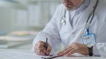 Male Doctor Filling Out Documentation Form at Desk in Clinic
