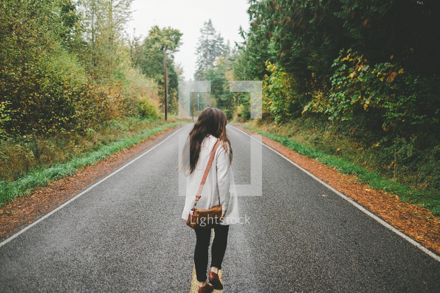 a woman walking down the middle of a road 