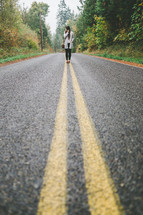 A woman standing on double yellow lines in the middle of a highway.