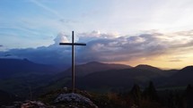 Aerial view of a Christian cross on a rock in a mountain rural landscape at sunset