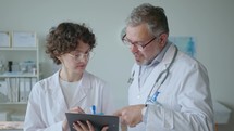 Young Female Doctor Writing Medical Record under Guidance of Senior Colleague
