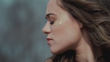face of a young woman with gold glitter on her face 