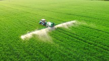 Aerial top view of farming tractor plowing and spraying on agriculture large territory greenfield. Machinery equipment for assistance a farmland. Cultivation greenery and plants big scale. Sprinkler.