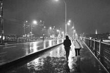 Two people walking over a bridge during a stormy night