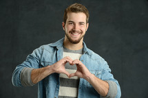 Casual young man making a heart shape with his hands against a gray background