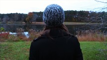 woman standing by a pond looking out at fall colors 