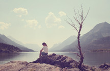 woman sitting on a rock at a lake shore 