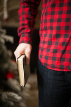 torso of a man in a plaid shirt holding a Bible at his side 