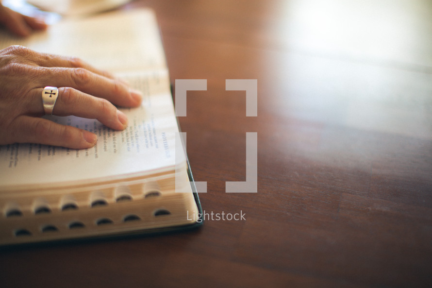 Hands on pages of open bible on wooden table.