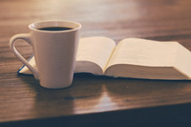  open Bible and coffee mug on a wood table 