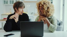 Two Young Female Friends Using Laptop and Talking at Home
