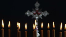 Small silver crucifix near lighting candle.
