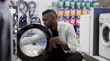 Black man is choosing washing machine in home appliances store, viewing exhibition sample.