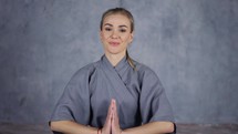 Smiling female coach yoga in robe makes Namaste gesture by hands.