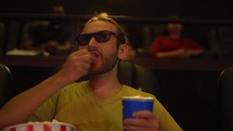 A man in 3d glasses watching comedy movie at the cinema and eating popcorn.