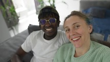 Joyful interracial couple taking selfies with smartphone while sitting together on sofa.