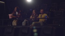 Group of young friends in a movie theater, came watching a movie on a big screen.