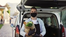 A movement shot of a delivery man wearing protective face mask carrying vegetables standing outdoors on the street. Corona virus or COVID 19 epidemic or pandemic.